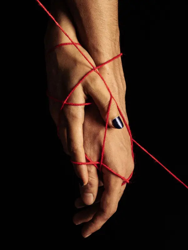 A Red String Tangles Around Two Hands Holding Together